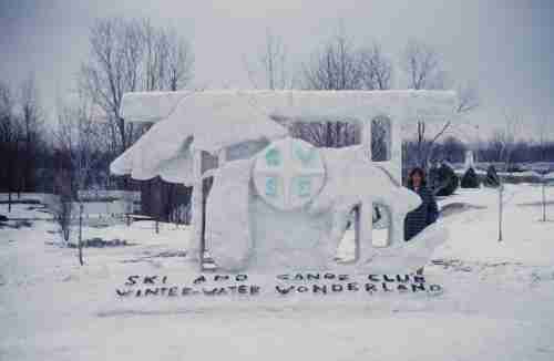 David stands behind an ice sculpture of the great lakes and Michigan along with the GVSC crest. The words "Ski and Canoe Club Winter Water Wonderland" are written below in black letters on the snow.